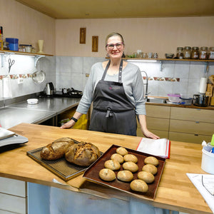 Rebecca steht hinter ihren zwei selbstgebackenen Broten und Brötchen