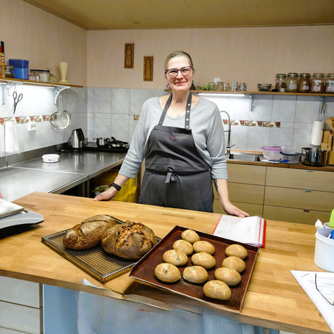 Rebecca steht hinter ihren zwei selbstgebackenen Broten und Brötchen