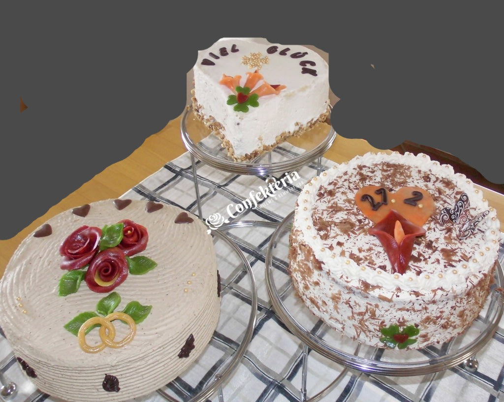 Die hintere Torte ist ein Herz, mit Callas und den Worten: viel Glück. Rechts vorne eine Schwarzwälder Kirschtorte mit feinen Schokospänen. Links vorne Mokkasahne mit roten Marzipanrosen und goldenen Ringen