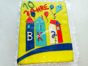 rechteckige Torte mit gelber Marzipandecke, darauf sind drei Häuser, Luftballons und die Buchstaben BKJ 