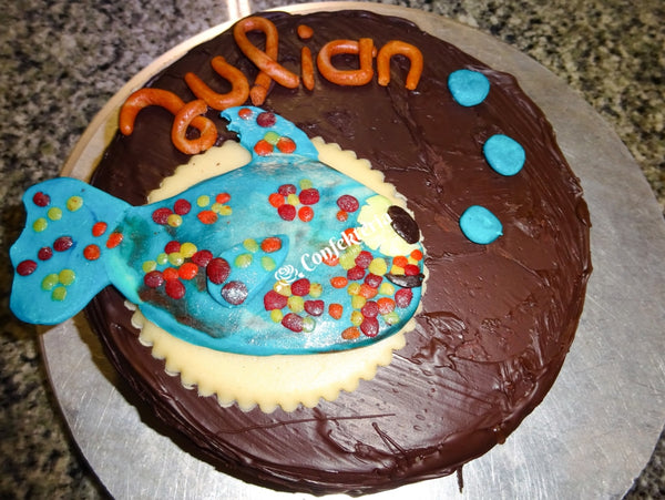 Auf der Torte steht der Name Julian, vorne liegt ein blauer Fisch mit bunten Tupfen. Alles aus Marzipan