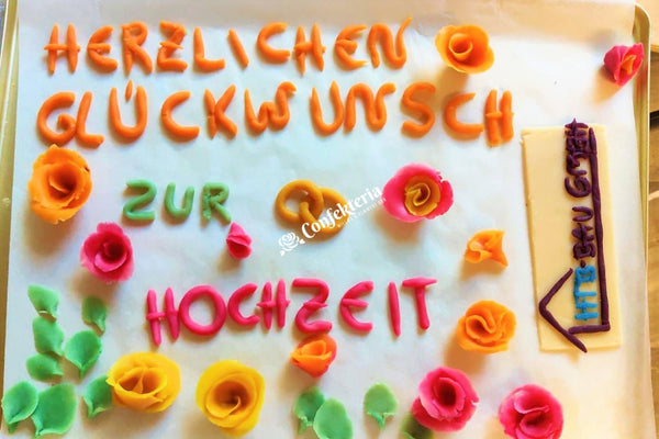 blick auf die einzelnen Marzipandekoelemente, die die Torte zieren werden. Ein Schriftzug und einige Rosenblüten und Blätter.